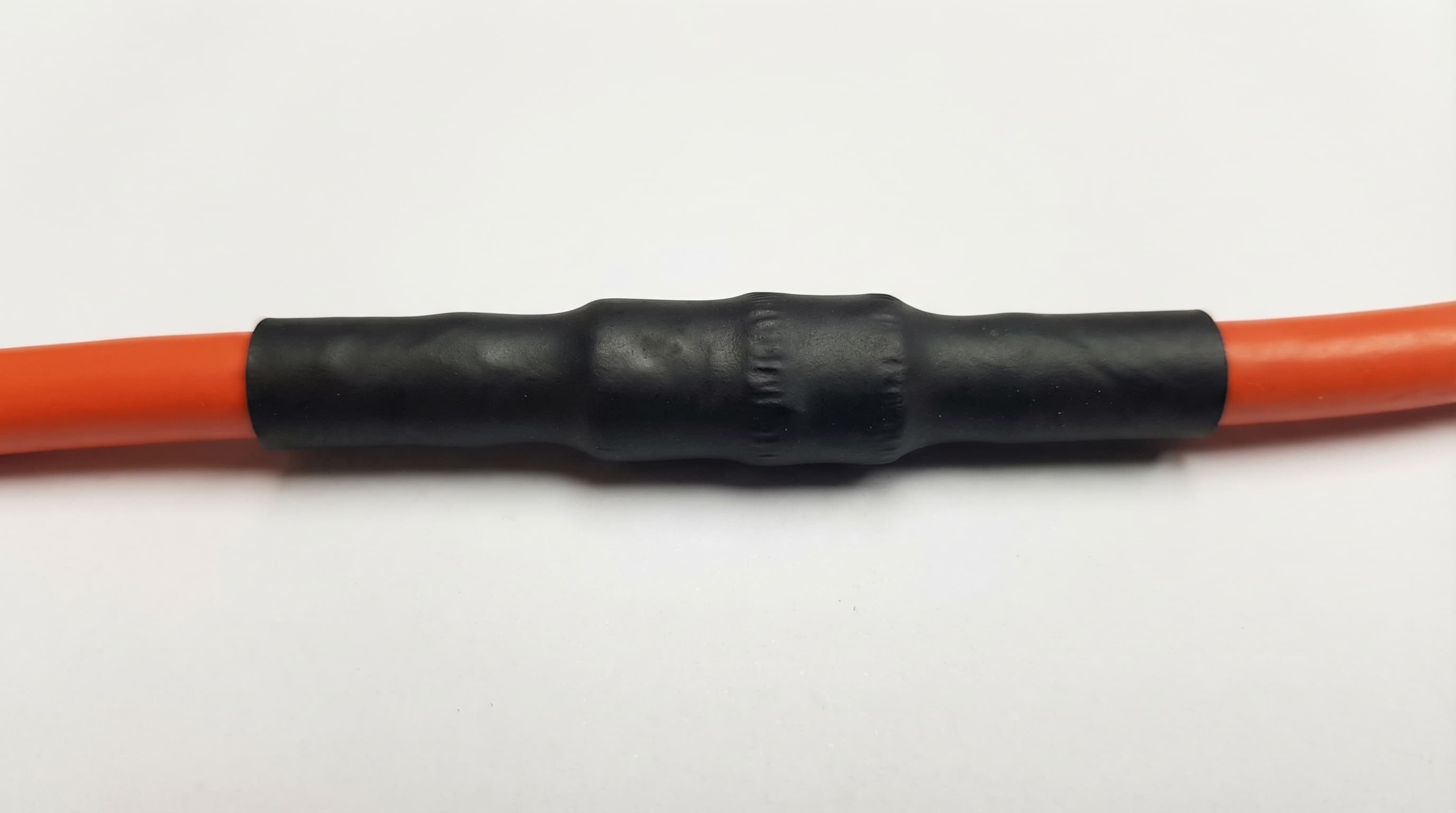 Correctly installed dual wall adhesive lined heat shrink tubing on an orange wire — fully shrunk with adhesive bead visible at ends confirming a complete waterproof seal